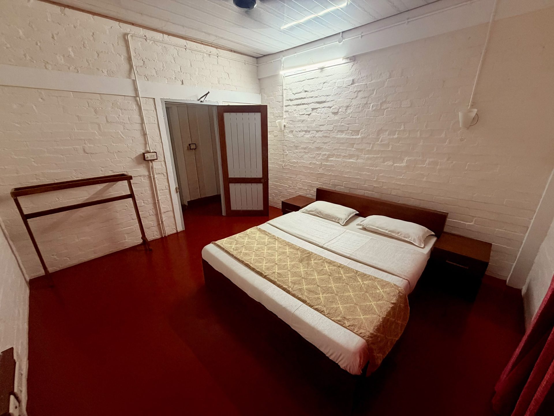 Poomukham room with a dark red floor, whitewashed brick walls, and a wooden bed